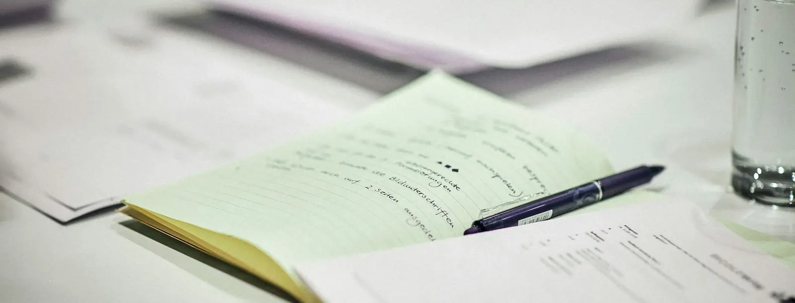 Papers and a pen on a desk beside a glass of water