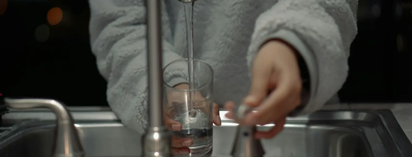 Person filling a glass at a kitchen sink at home